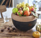 Deep ceramic storage bowl with cork lid, filled with assorted fresh fruit and nuts on a wooden table