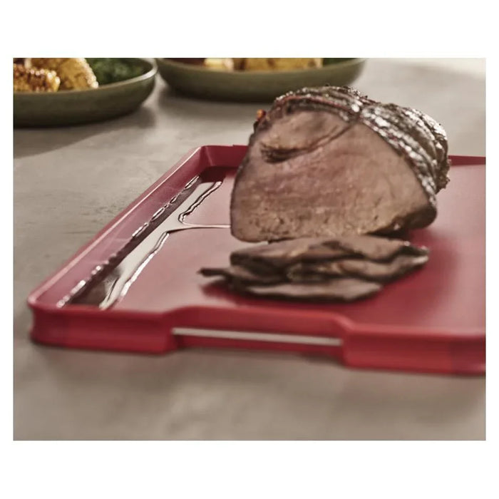 Red cutting board with grooves holding sliced roast beef on kitchen counter