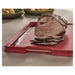 Red cutting board with grooves holding sliced roast beef on kitchen counter
